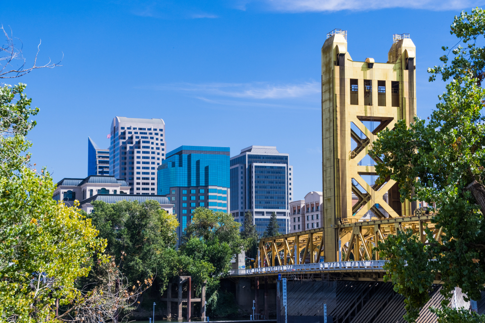 Skyline of Sacramento showing a bridge in the foreground and tall buildings in the background, with a few trees in the middle distance.